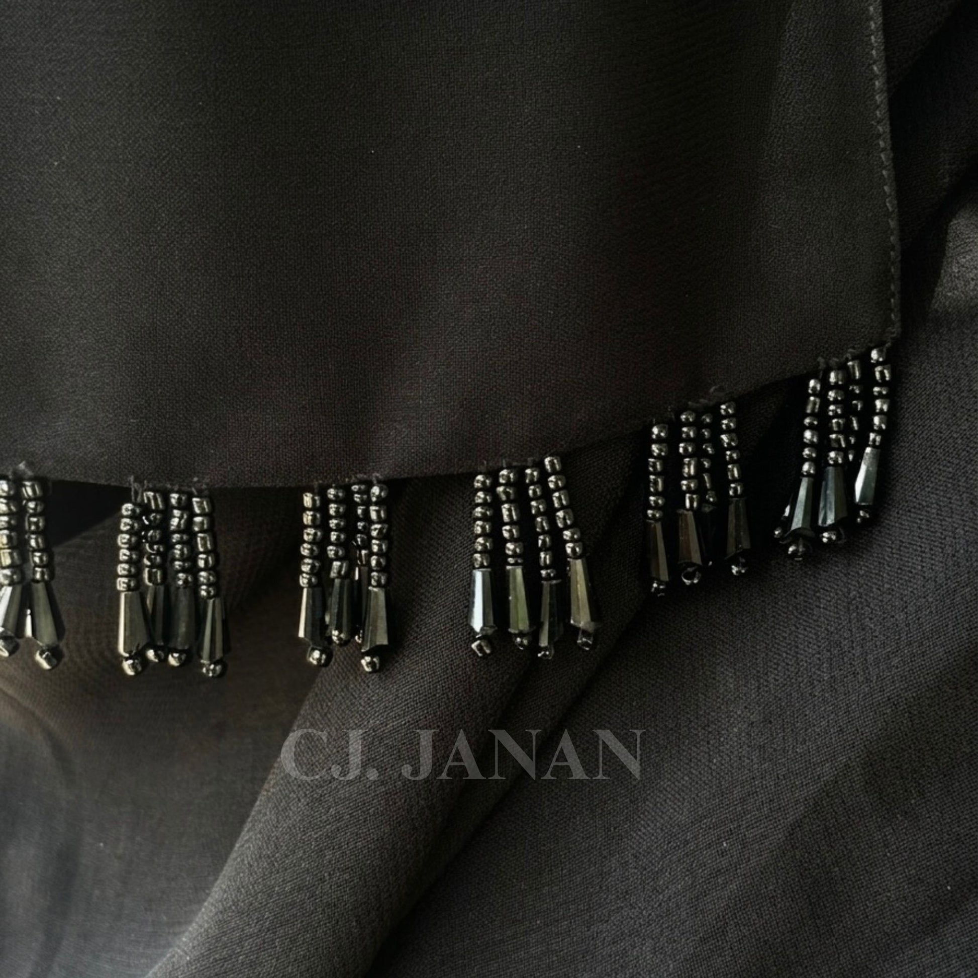 Black fabric with beaded fringe detail, featuring the brand 'C.J. Janan'.